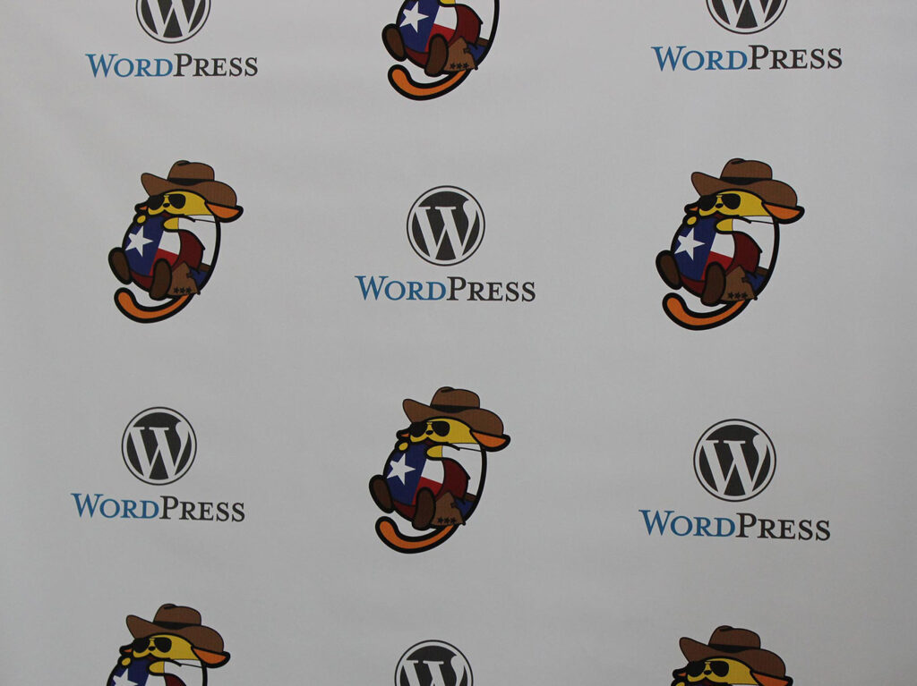 Step and repeat banner with the WordPress logo and the Cowboy Wapuu
