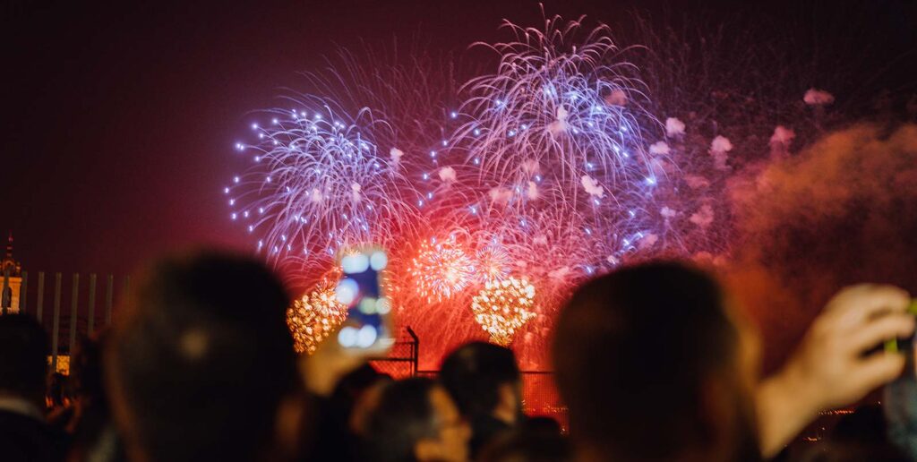 A mix of red and blue fireworks as a crowd watches on
