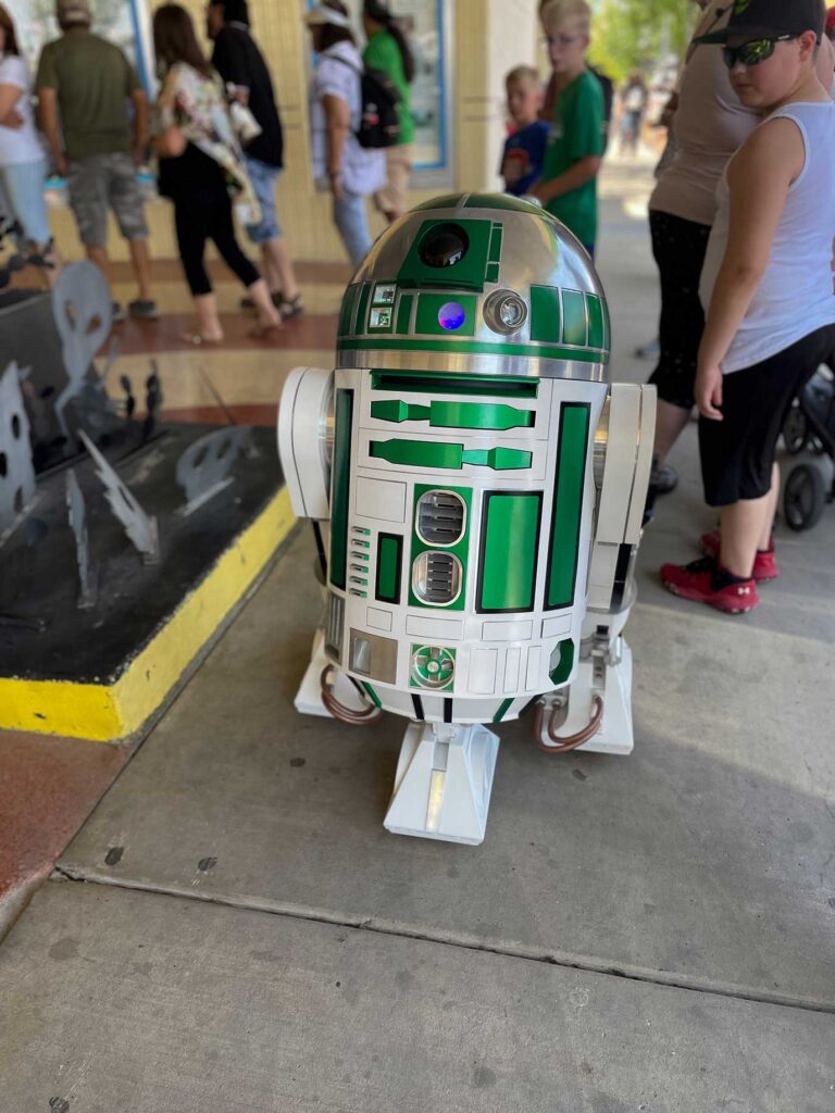 A green R2 unit from Star Wars moving through a line of people