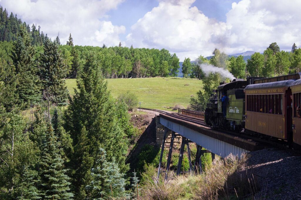 A steam engine leads a train over a bridge