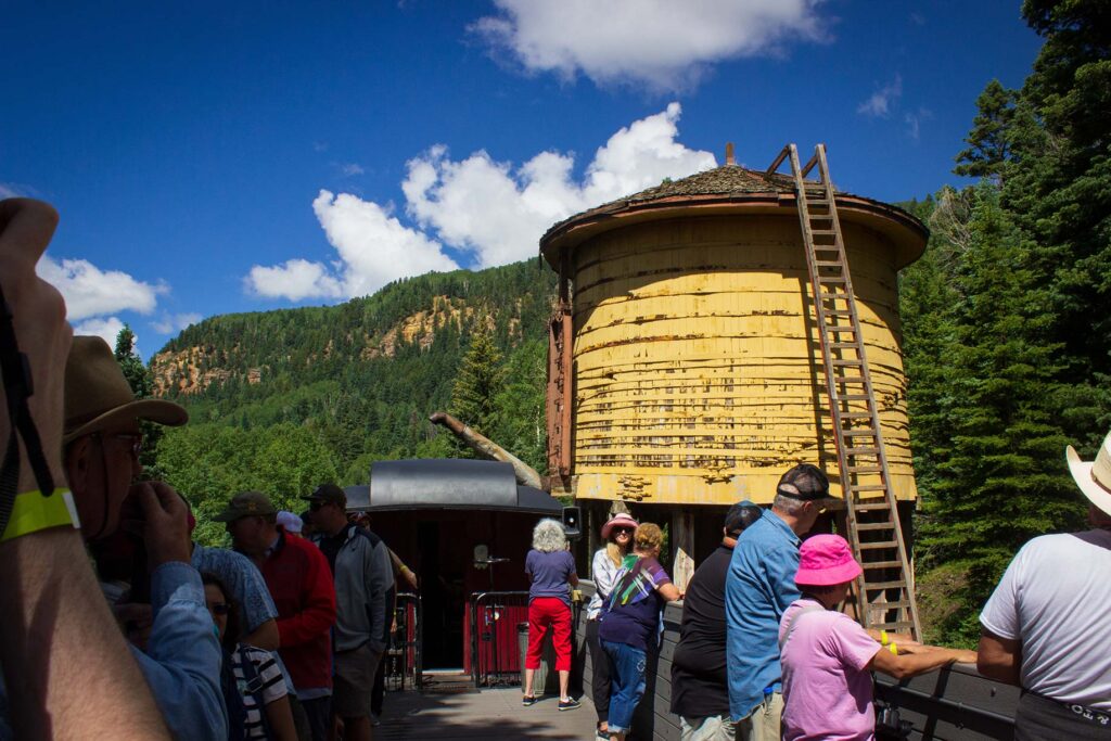 People standing in a gondola car passing next to a yellow water tower