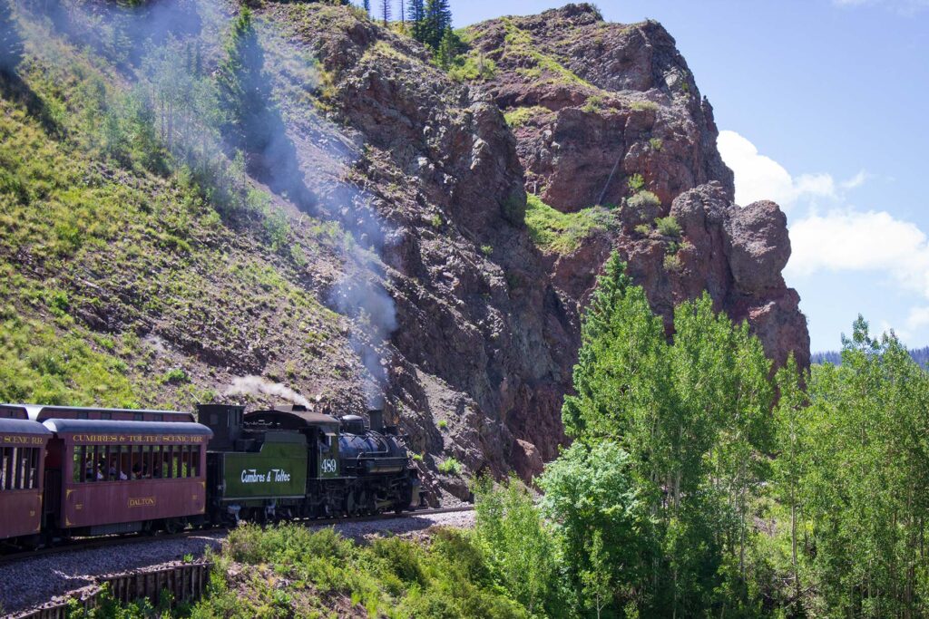 A train travels in the mountains along a cliff face