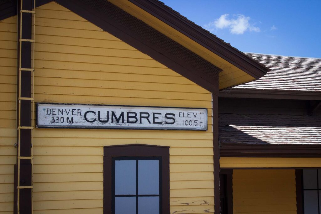 A yellow station building with a sign reading "Cumbres"
