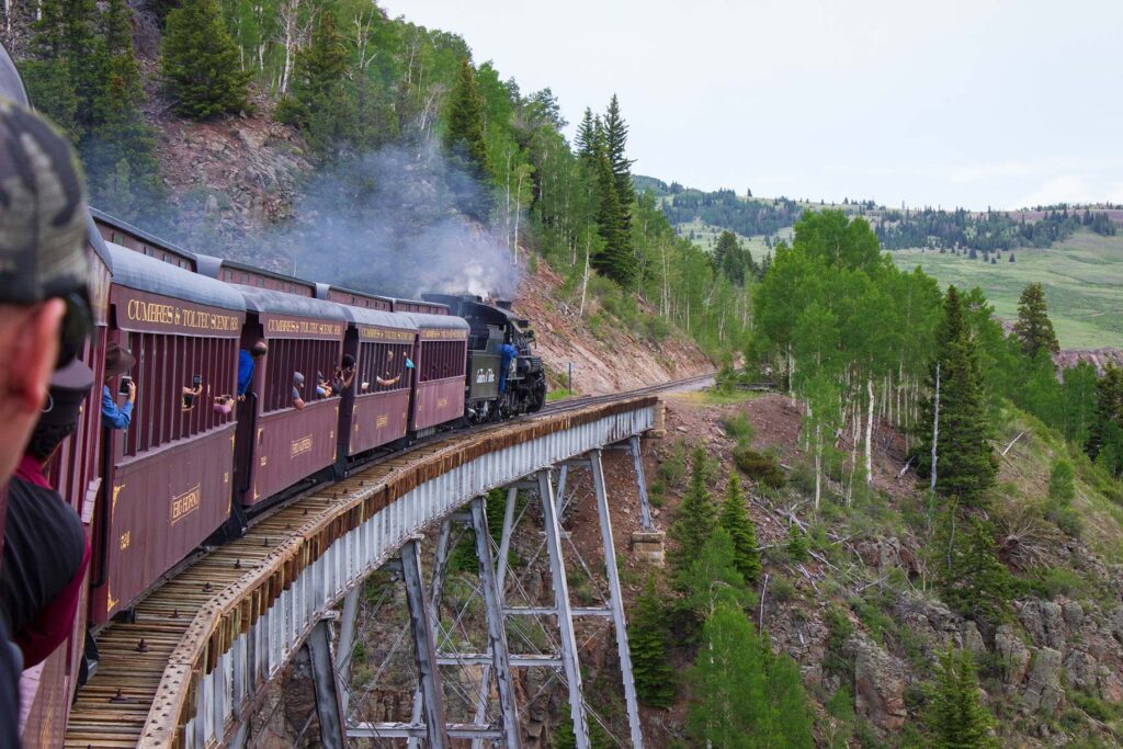 A steam train leading a train over a bridge in the mountains