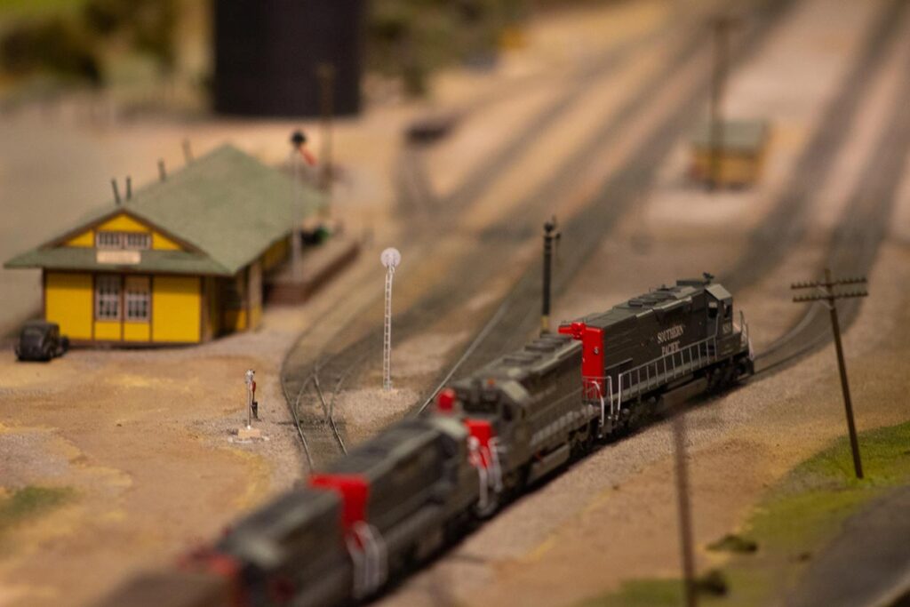 A Southern Pacific train running passed a yellow depot on a model train layout