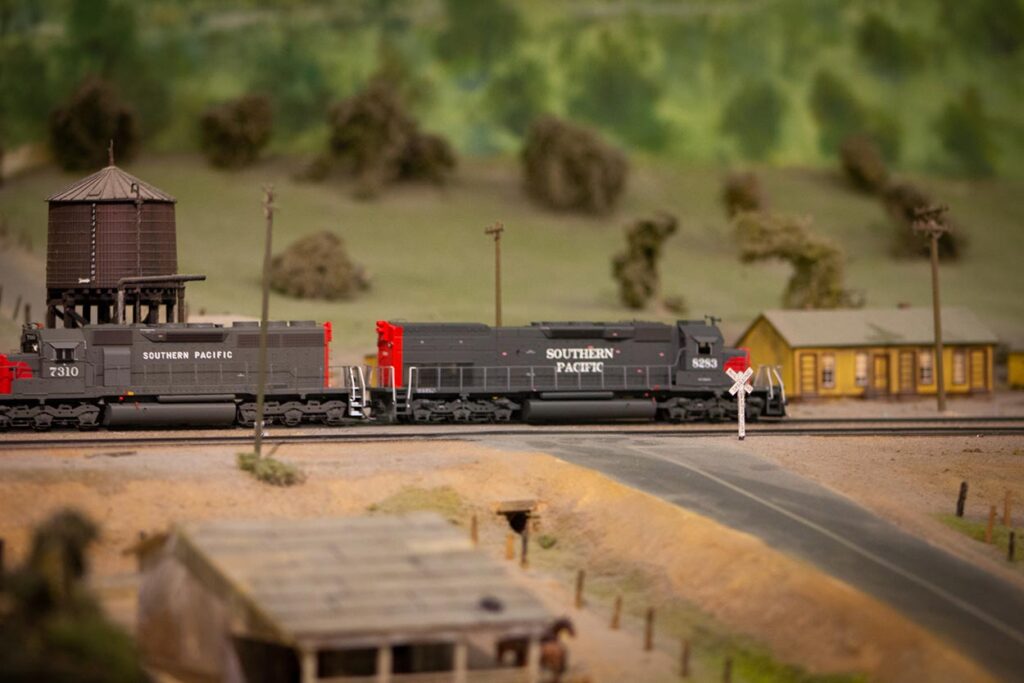 A Southern Pacific training running passed a grade crossing and some buildings on a model train layout