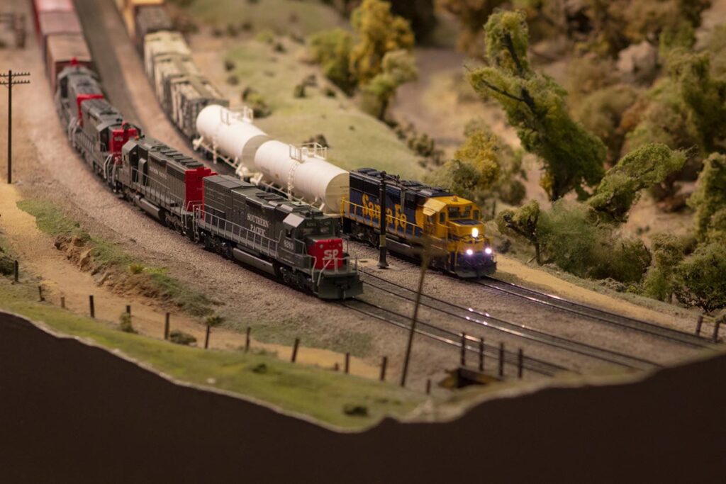 A blue and yellow Santa Fe train running passed a Southern Pacific train on a model train layout