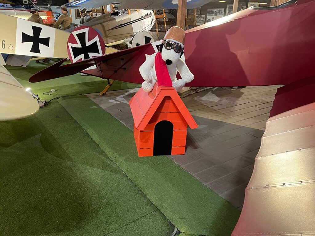 Snoopy dressed as the Red Barron sitting on a dog house surrounded by World War I airplanes