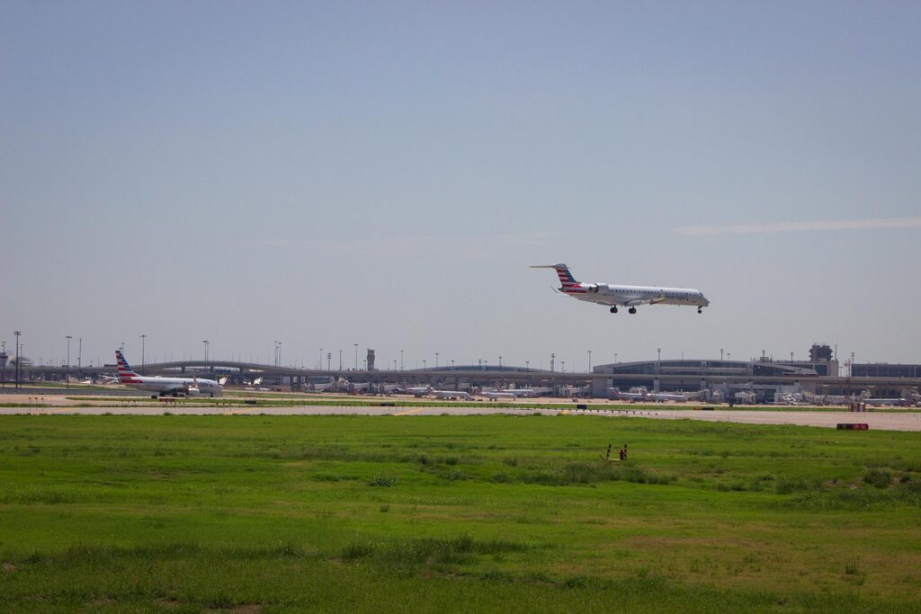 A smaller American Airlines plane lands while a larger American Airlines plane waits to take off in the background