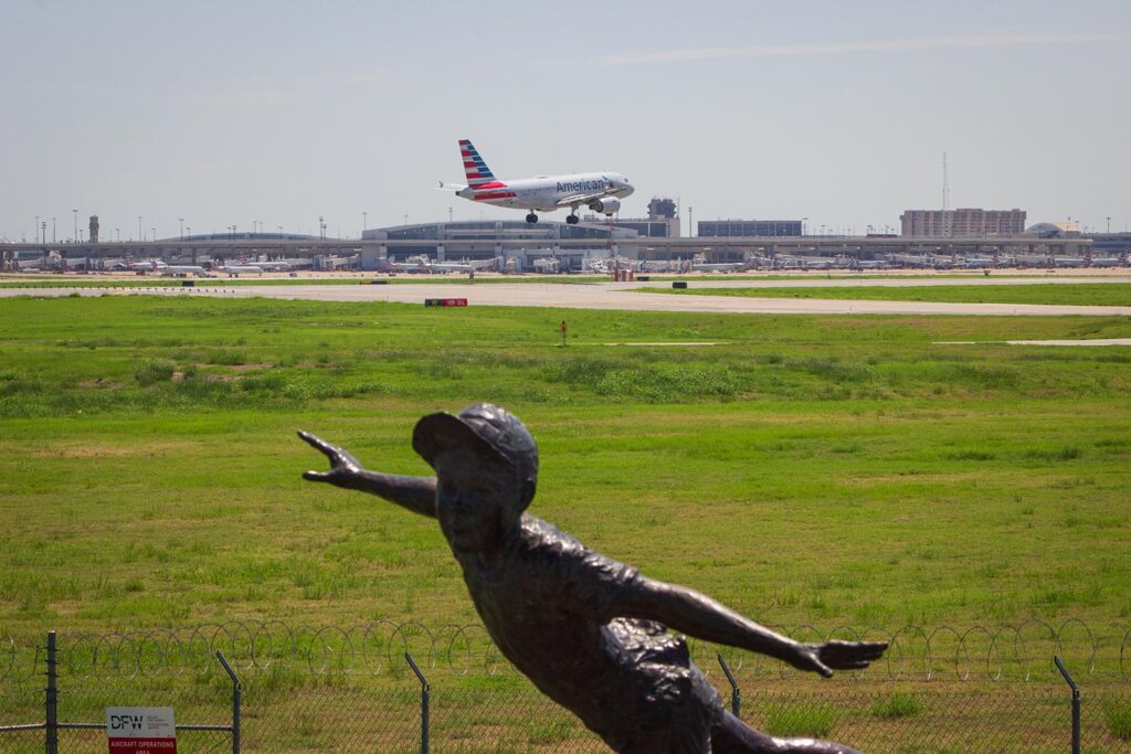 An American Airlines plane lands in the background with a statue of a boy in the foreground