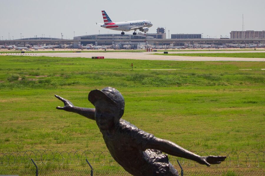 An American Airlines plane lands in the background with a statue of a boy in the foreground