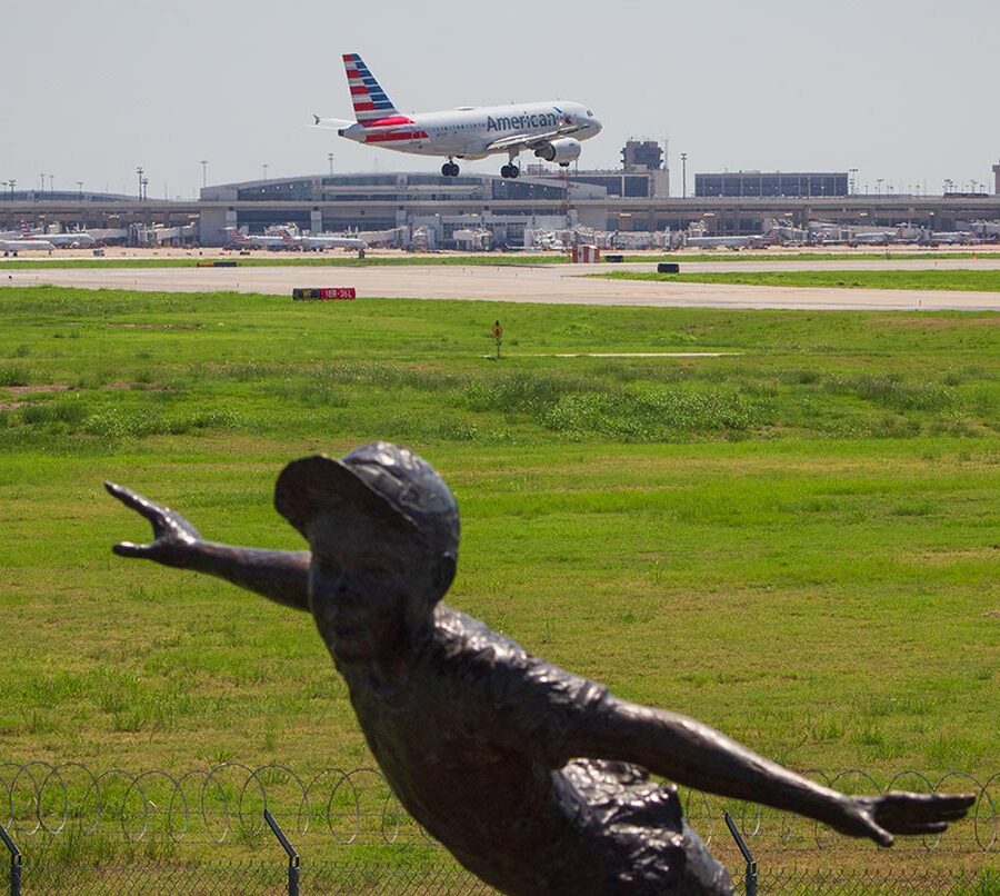 An American Airlines plane lands in the background with a statue of a boy in the foreground