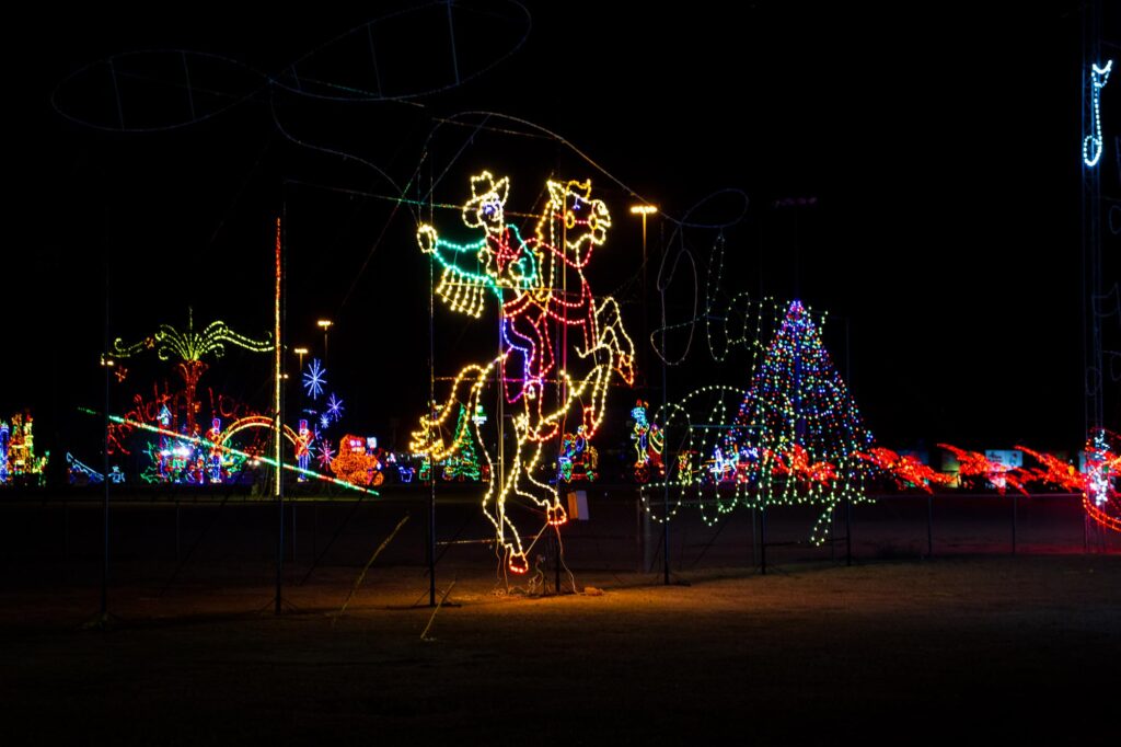 Colored lights in a park at night depicting a Cowboy writing "Happy Holidays" with his lasso