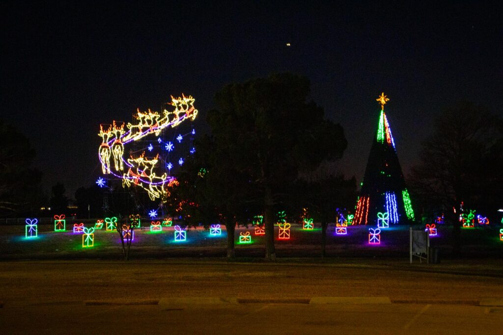 Colored lights in a park at night depicting presents, a Christmas tree and reindeer