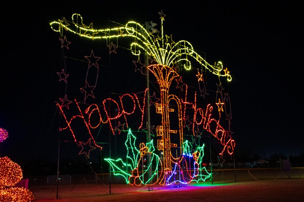 Colored lights in a park at night depicting a sign saying "Happy Holidays"