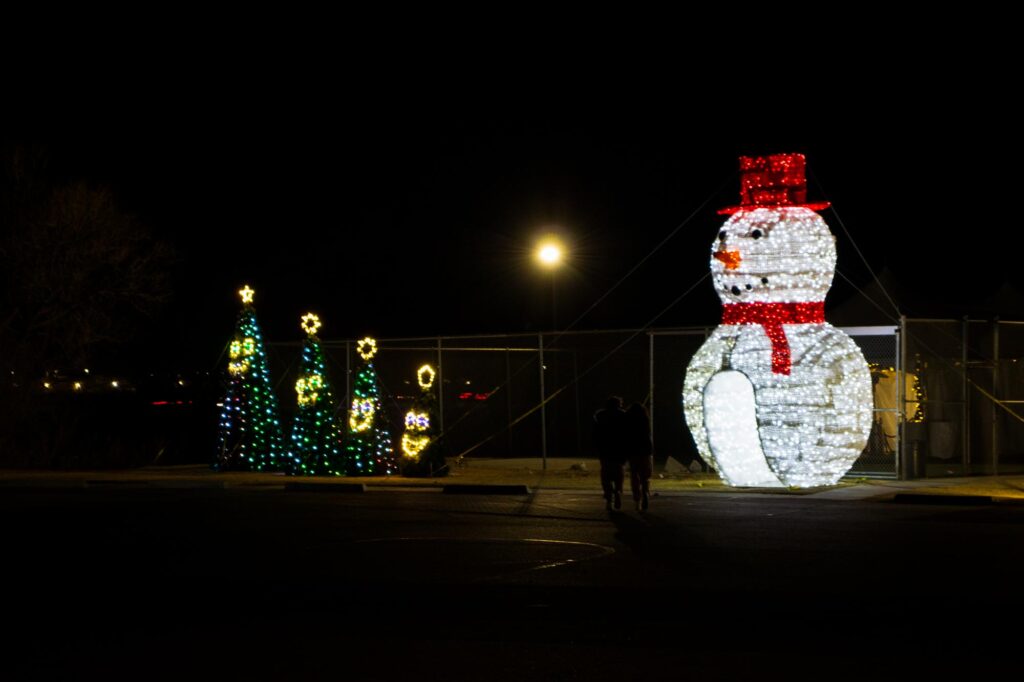 Colored lights in a park at night depicting a snowman and four singing Christmas tree