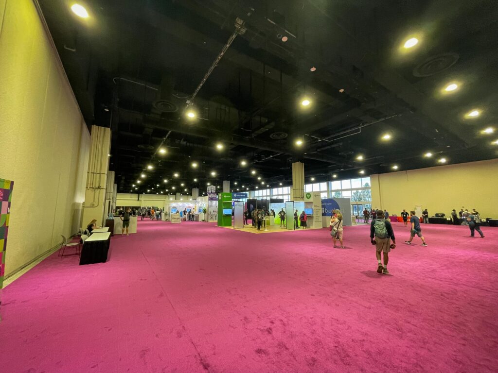 A large convention center room with sponsor booth and a pink carpet