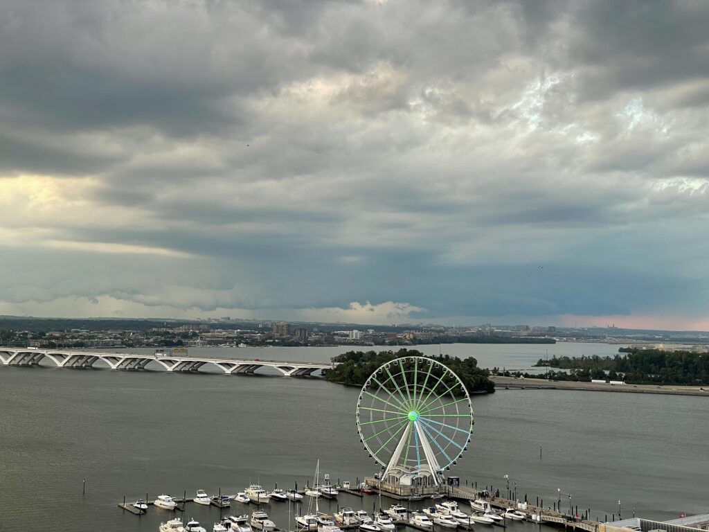 A ferris wheel lit up with a river behind and storm clouds overhead