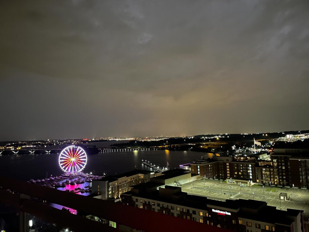 A ferris wheel lit up at night with a river behind and storm clouds overhead
