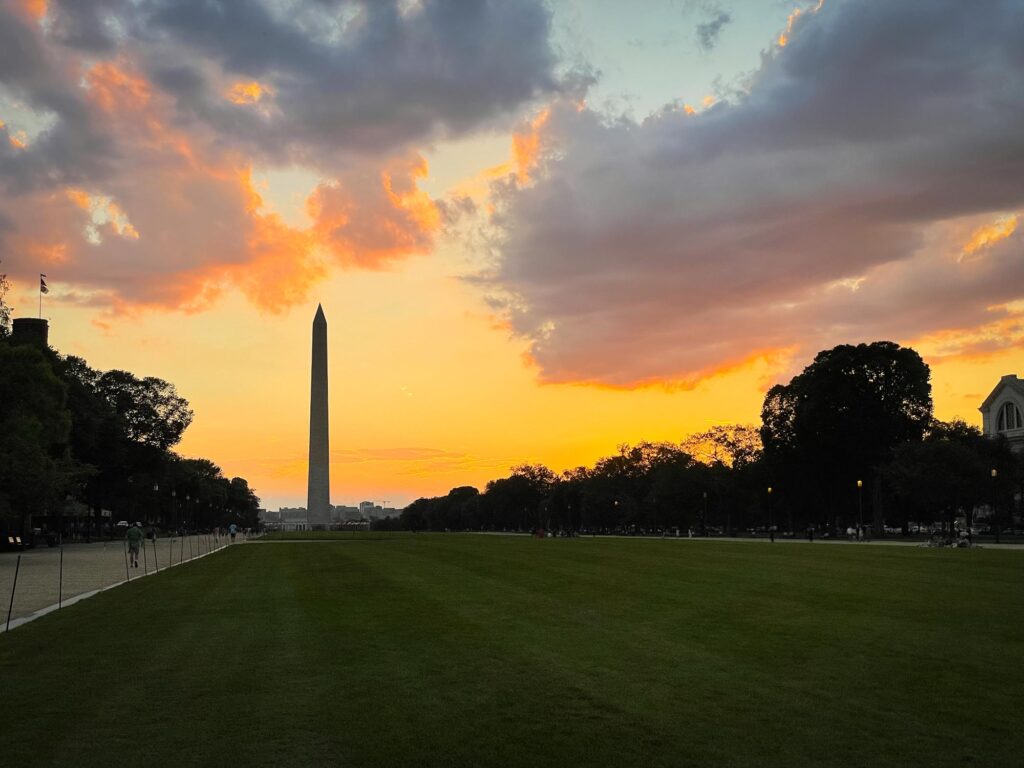 The silhouette of the Washington Monument with an orange and purple sky and clouds overhead
