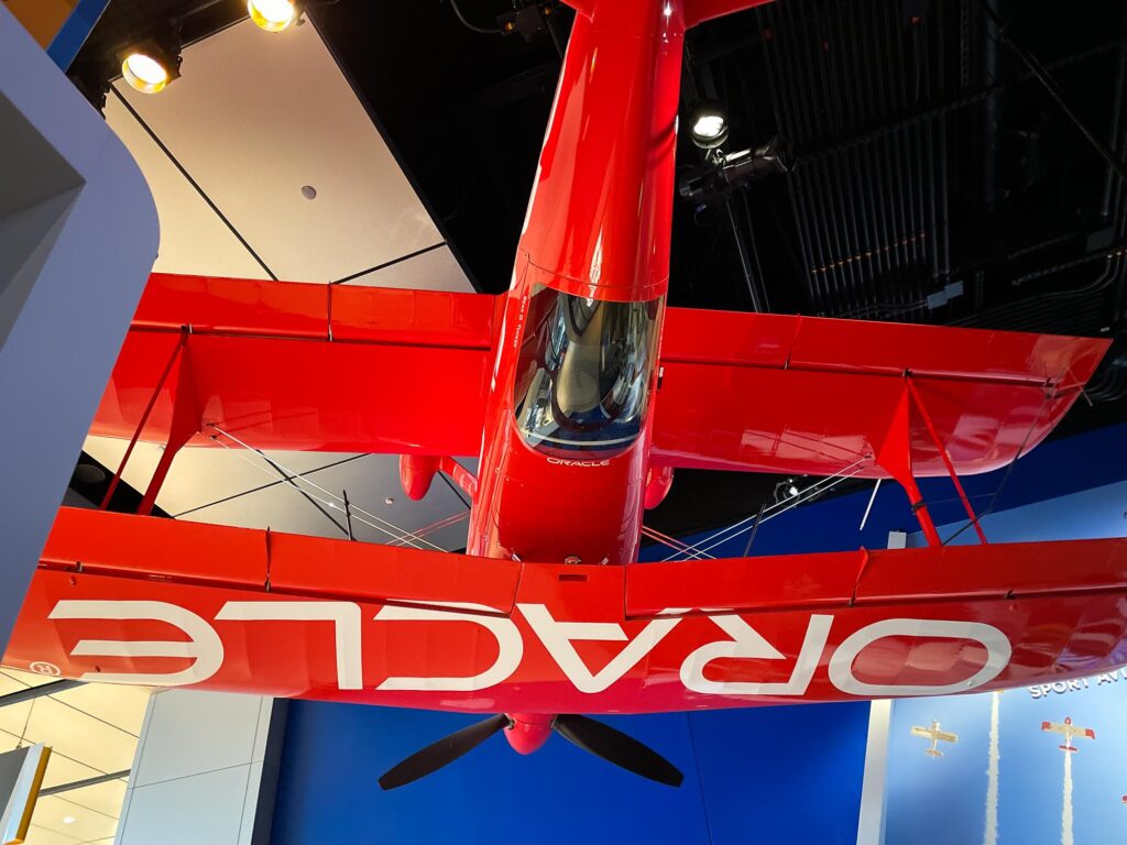A red biplane hanging upside down in a museum