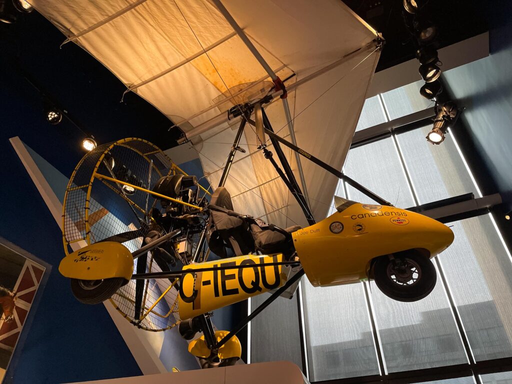 A yellow ultralight plane hanging in a museum