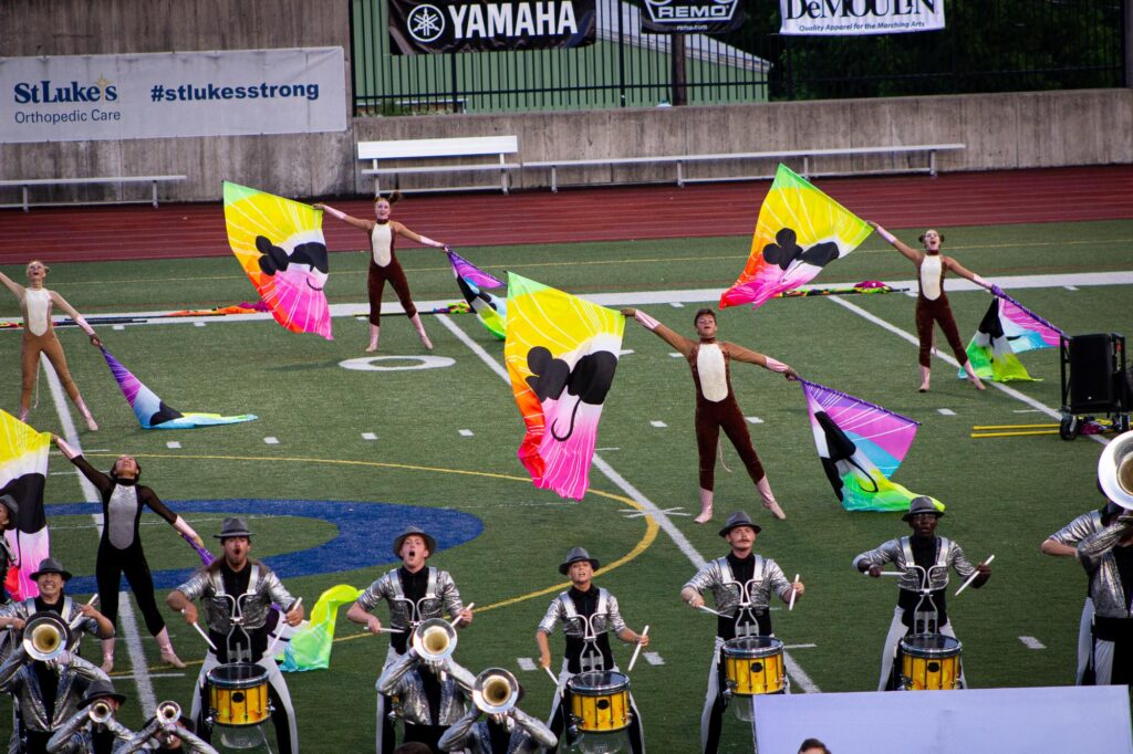 A drum corps color guard performing on the field with rainbow silk flags