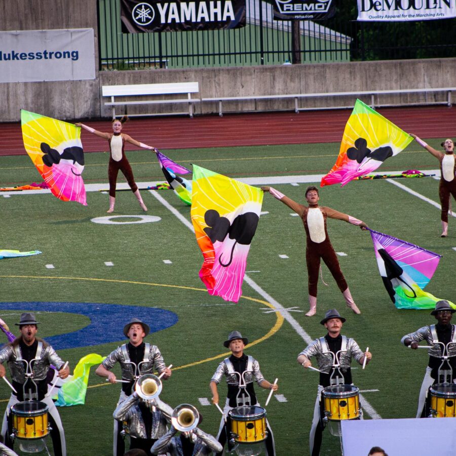 A drum corps color guard performing on the field with rainbow silk flags