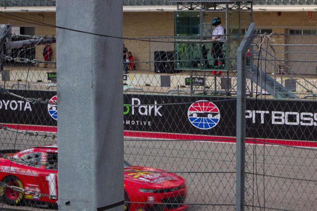 A flag man watches as a red stock car drives by on a racetrack