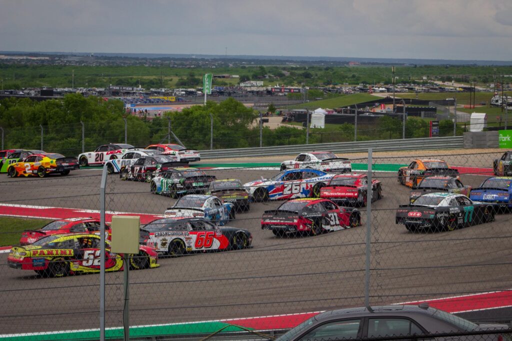 Stock cars racing on a racetrack at a tight turn with one car spinning