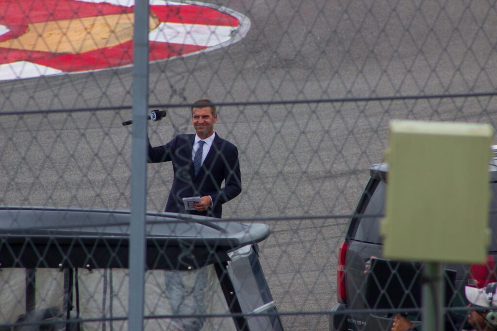 A person in a suit waving to the crowd at a race track