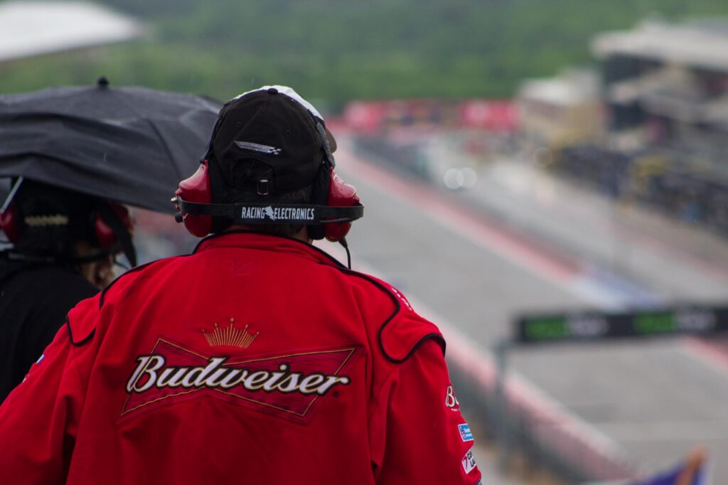 Person wearing racing headphones and a red Budweiser jacket