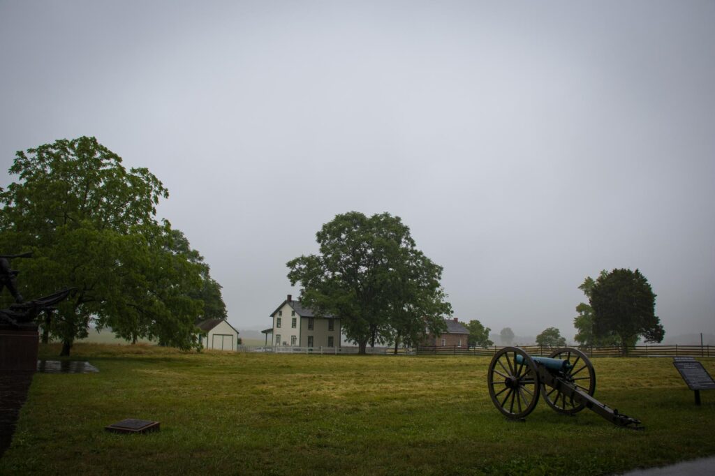 A civil war era cannon with a couple of farm buildings in the background