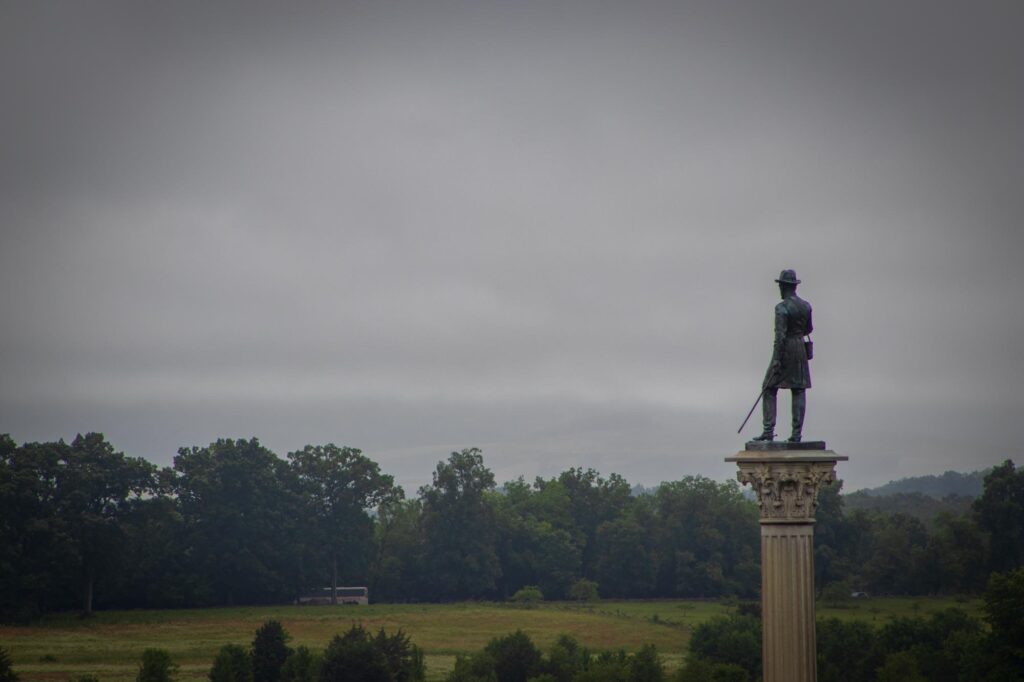 A statue of a civil war soldier with a sword on top of a pillar looking away from the camera