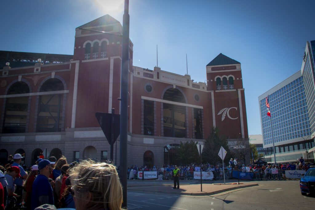 The facade of a baseball stadium with people lining up for a parade outside of the stadium