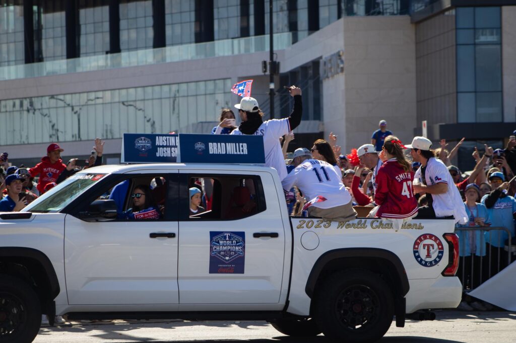 People in Texas Rangers jerseys and jackets in the back of a pickup truck in a parade