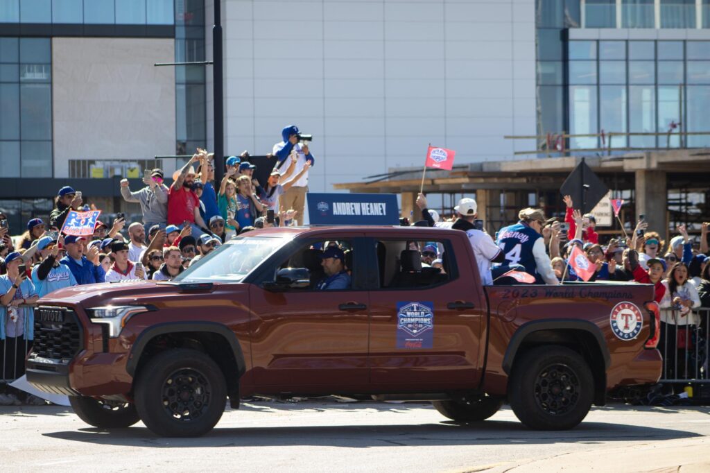 People in Texas Rangers jerseys and jackets in the back of a pickup truck in a parade
