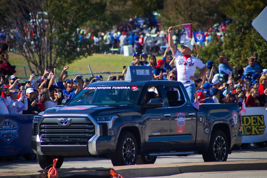 A man in a Texas Rangers jersey standing in the back of a pickup truck in a parade