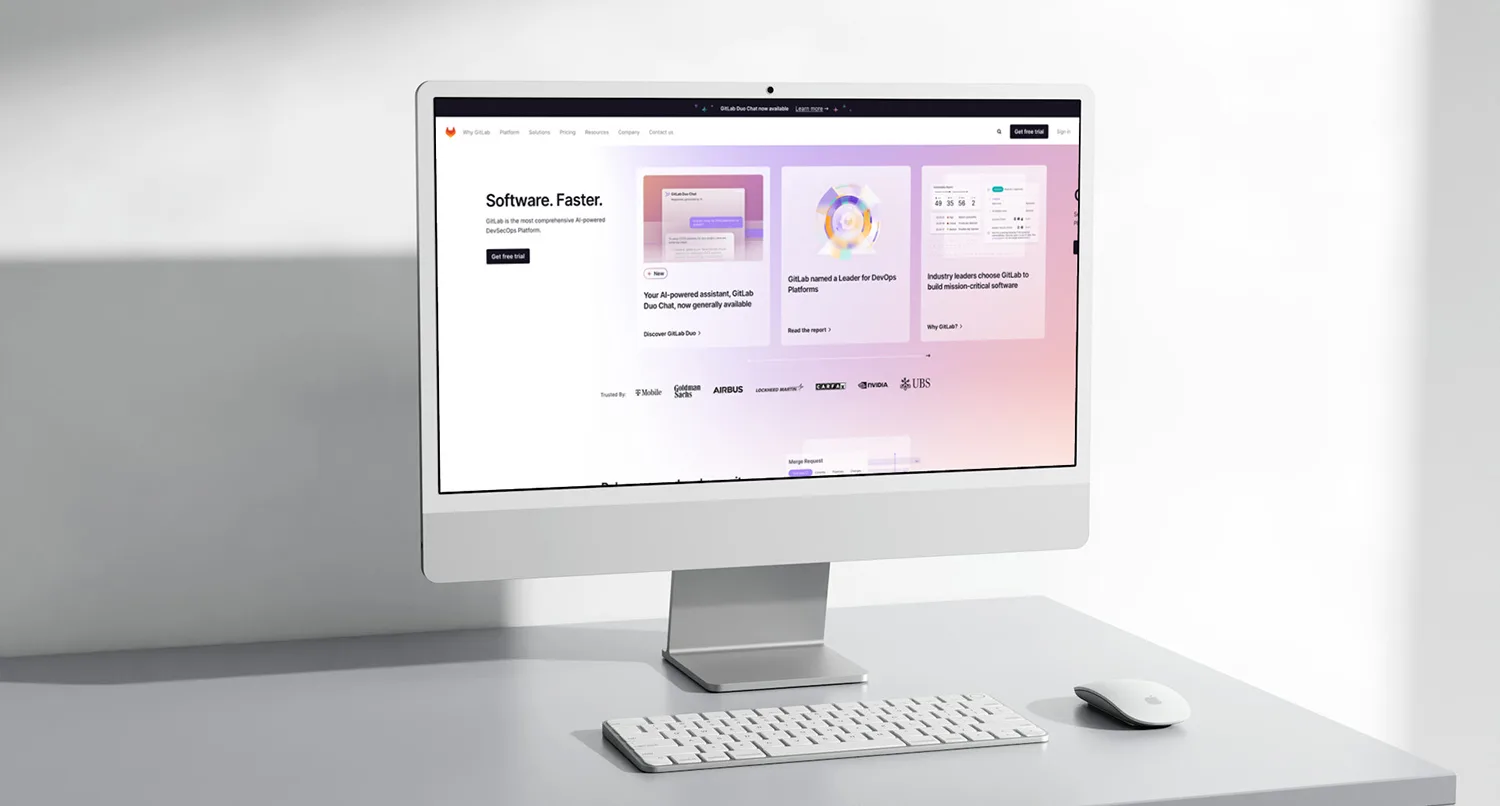 the GitLab homepage on an iMac sitting on a white desk in a white room
