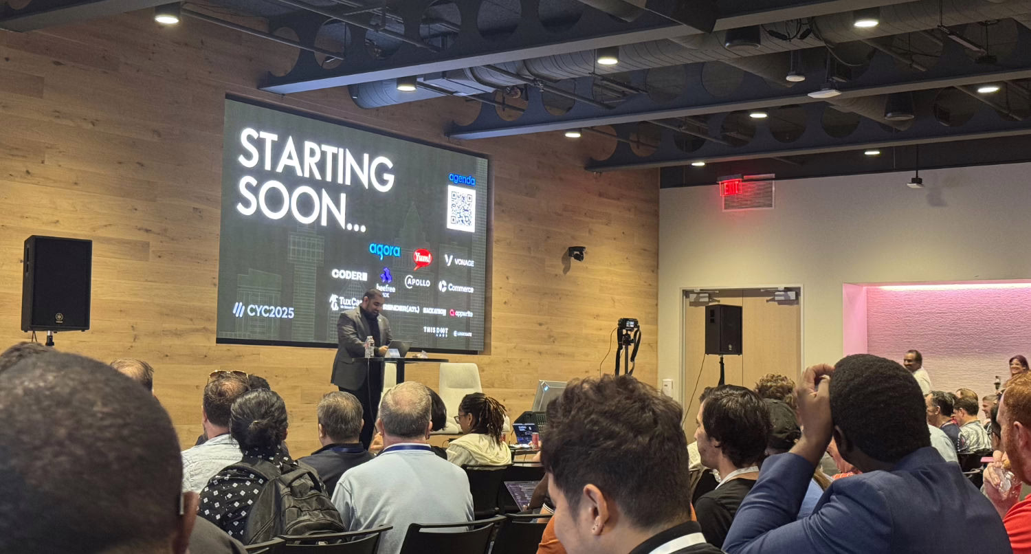 From the perspective of the audience, a Black man in a dark suit jacket stands on a stage, speaking at a small lectern. Behind him, a large screen on a wood-paneled wall displays "STARTING SOON..." in large white text, along with the event logo "// CVC2025" and various sponsor logos.